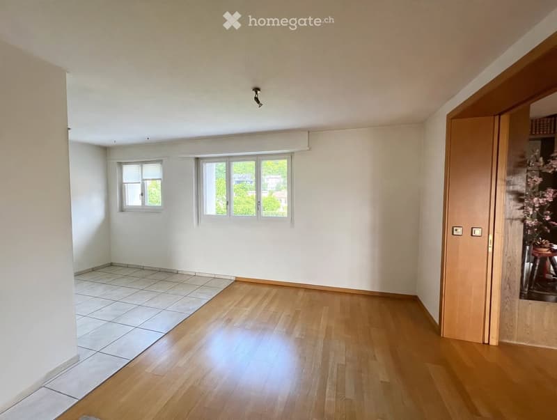 Empty room with light-colored walls, wooden flooring, and large windows allowing natural light. The space is unfurnished, showing only the basic structure and layout.