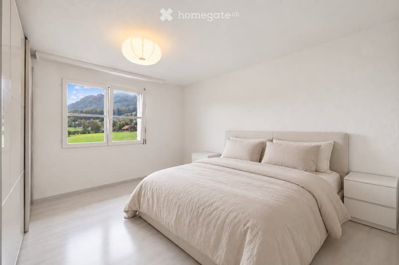 Modern bedroom with a large bed, nightstands, and a scenic view through large windows.