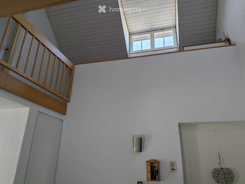 A modern hallway with white walls, wooden railing, and a window at the top of the stairs.