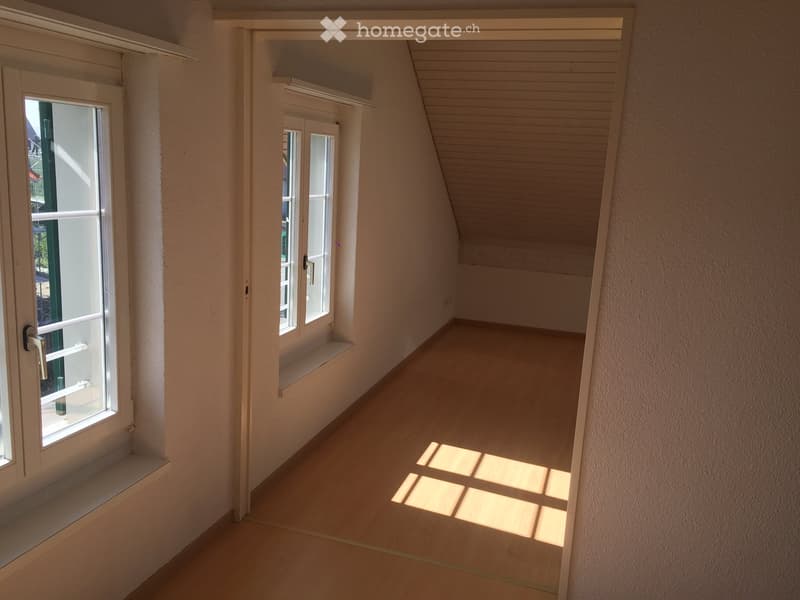 Empty hallway with wooden flooring, white walls, and natural light coming through windows on both sides.