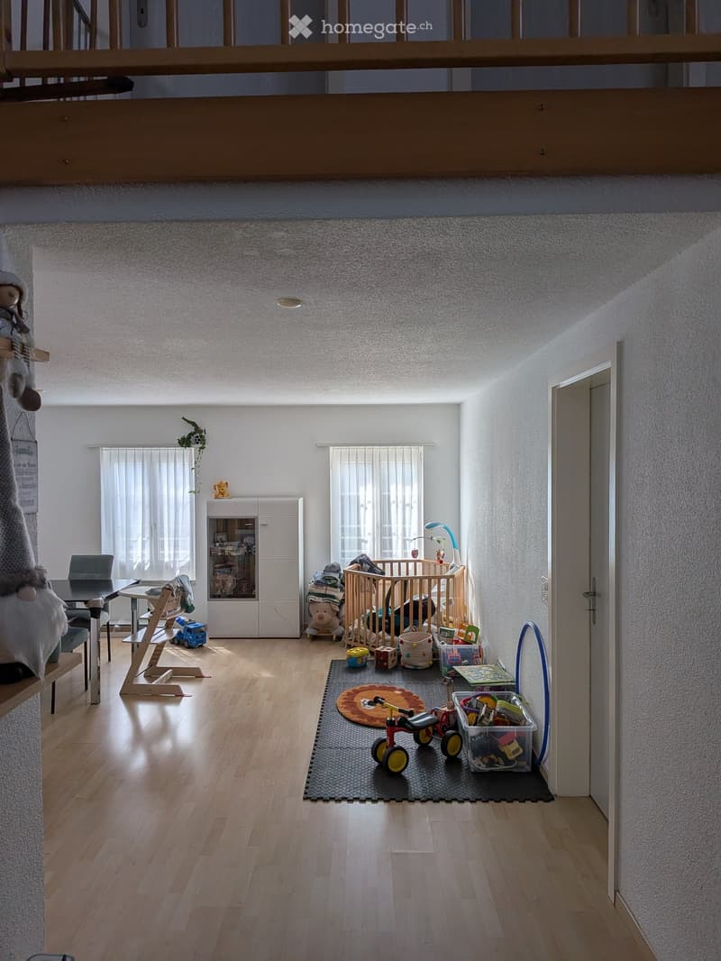 Bright, open living space with wooden flooring, a crib, toys, a small table, and a cabinet.
