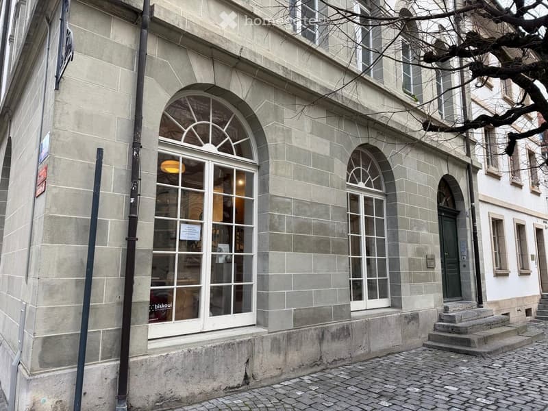 Exterior view of a multi-story building with stone facade, arched windows, and a sign indicating a rental space.