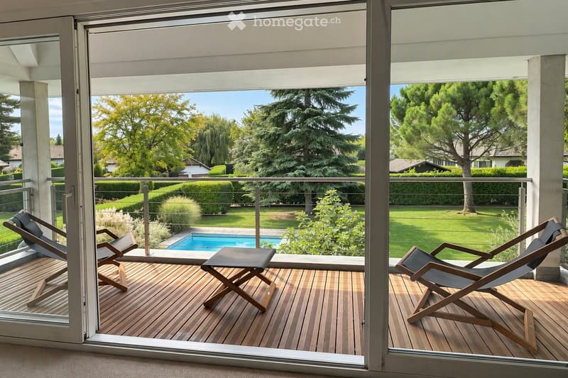 Balcony with wooden decking, several lounge chairs, and a view of a well-maintained garden and swimming pool.