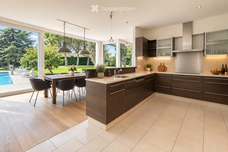 Modern kitchen with dark wood cabinets, a central island, pendant lights, and a dining area with a table and chairs. The kitchen features a sink, faucet, and various decorative items like vases and bottles. Large windows offer a view of a garden and pool