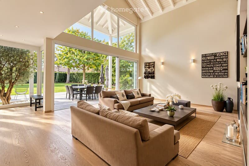 Modern living room with large windows, two sofas, coffee table, ottoman, dining area with table and chairs, and decorative vases.