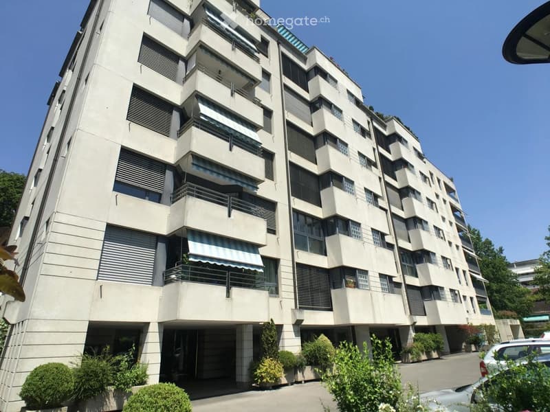 Modern multi-story residential building with balconies, large windows, and a mix of light-colored facades and dark window frames.