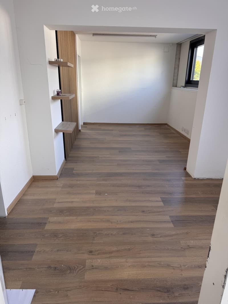Empty hallway with wooden flooring and white walls, featuring a small wooden shelf on the left side and a window on the right side.