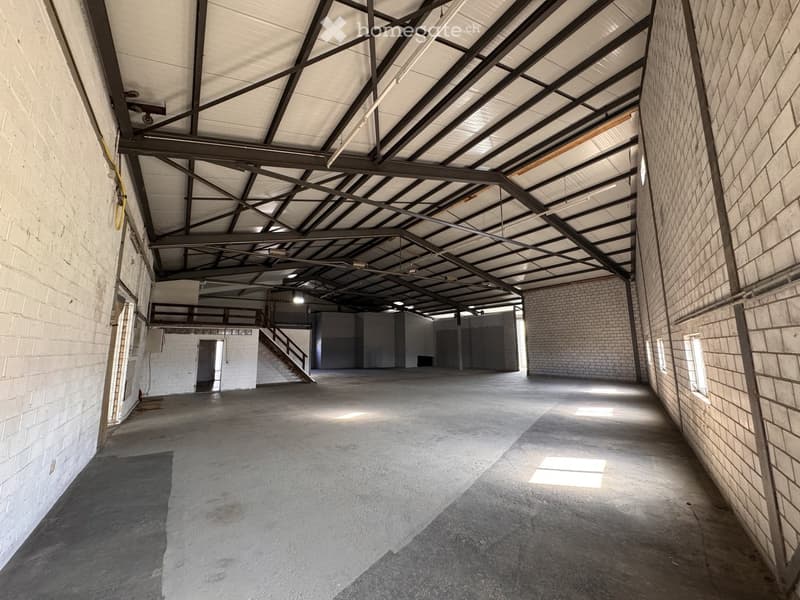 Empty industrial-style room with exposed metal beams, concrete floor, brick walls, and a staircase leading to an upper level.