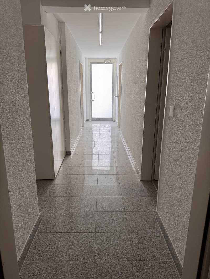 Empty hallway with tiled floor, white walls, and a glass door at the end.
