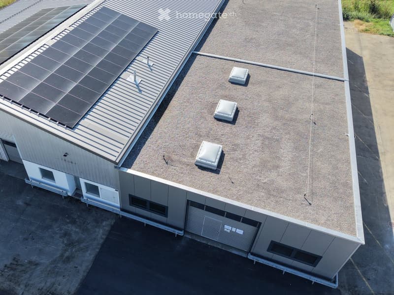 Modern industrial-style building with a flat roof, solar panels, and ventilation units.