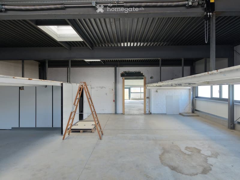 Empty industrial-style room with exposed metal beams, concrete floor, white brick walls, and a ladder in the corner.