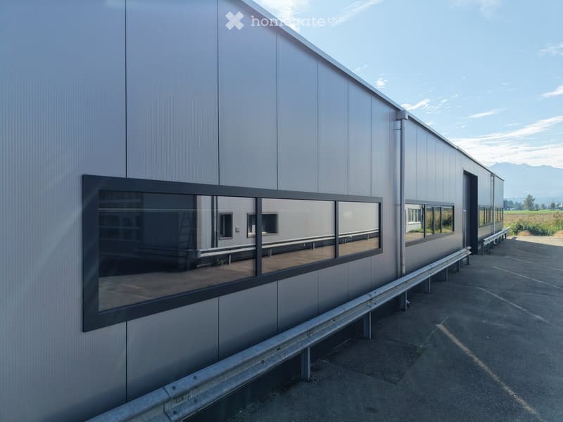 Modern industrial-style building with a metallic exterior, large reflective windows, and a paved area in front.