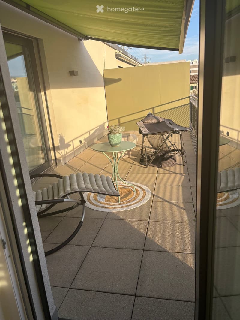 Balcony with tiled floor, small round table with a flower pot, lounge chair, and a baby chair.