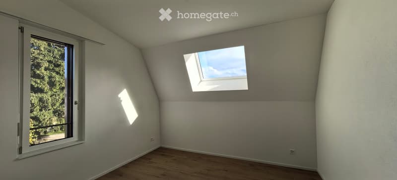 Empty attic room with wooden flooring, white walls, large window, and skylight allowing natural light.