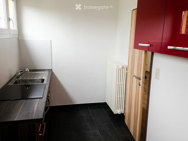 Modern kitchen with dark wooden countertop, stainless steel sink, red cabinets, white radiator, and black tiled floor.