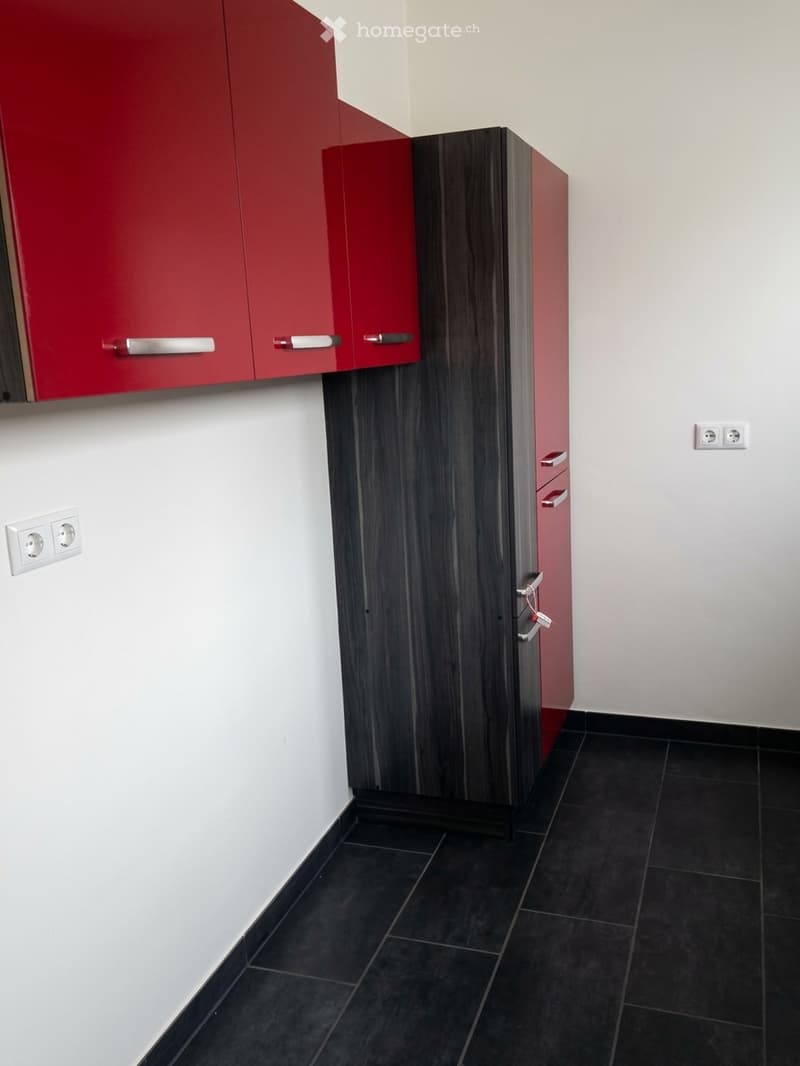 Empty room with white walls, black tiled floor, and fitted cabinets in red and dark wood finishes.
