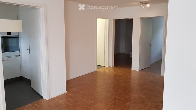 Empty hallway with wooden flooring, white walls, and several open doors leading to other rooms.
