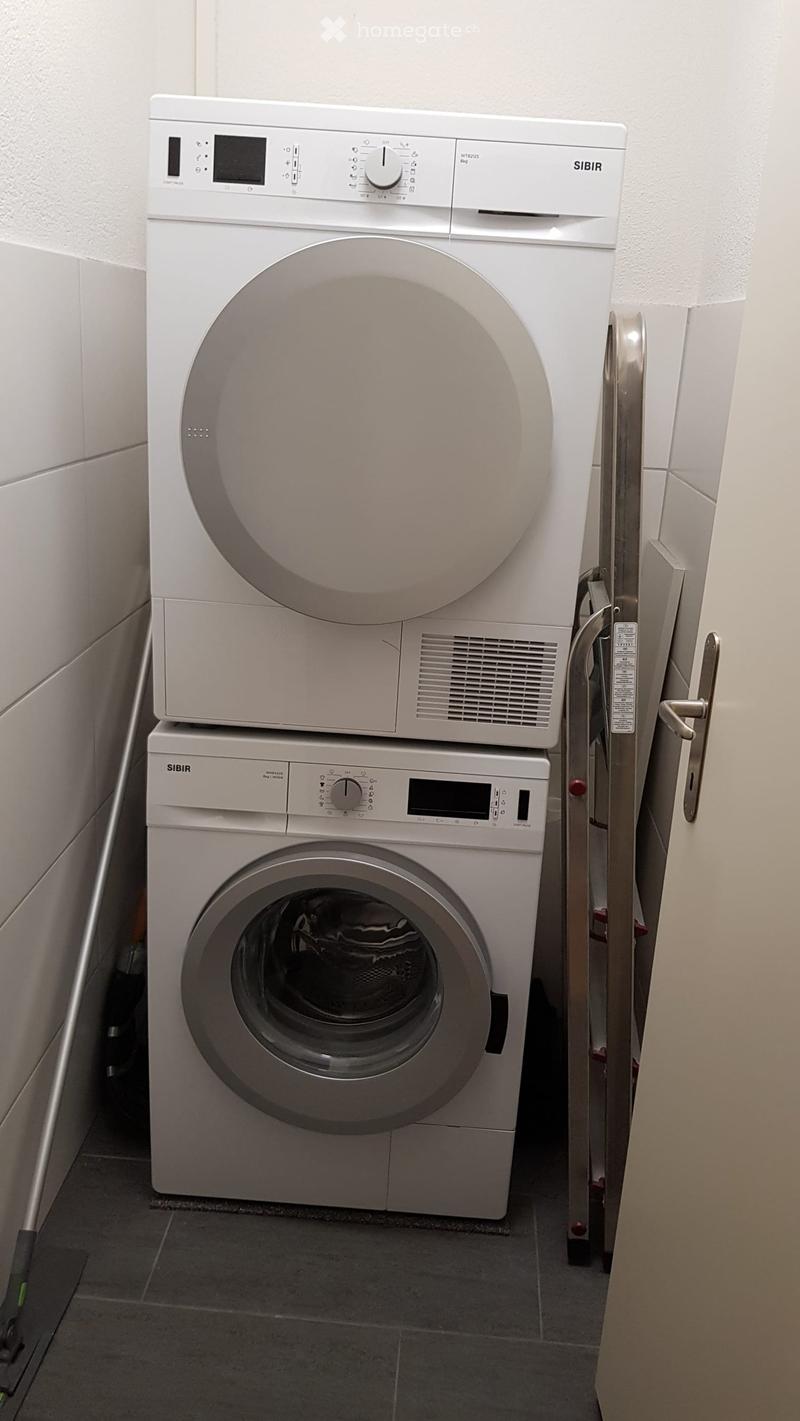 A compact bathroom with a stacked washing machine and dryer unit, white control panels, and a tiled floor.