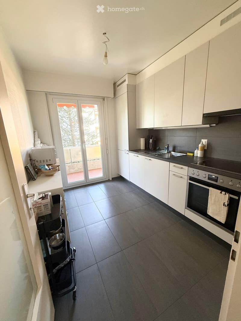 Modern kitchen with white cabinets, dark tiled floor, stainless steel appliances, and a sliding glass door leading to a balcony.