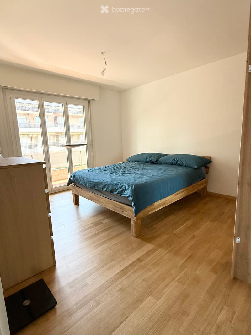 Minimalist bedroom with a wooden bed, blue bedding, and a nightstand near a large sliding glass door leading to a balcony.