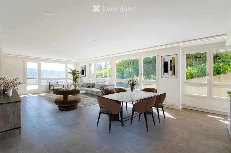 Bright, open living and dining area with large windows offering a scenic view, featuring a grey sofa, coffee table, dining table with chairs, and decorative vases.