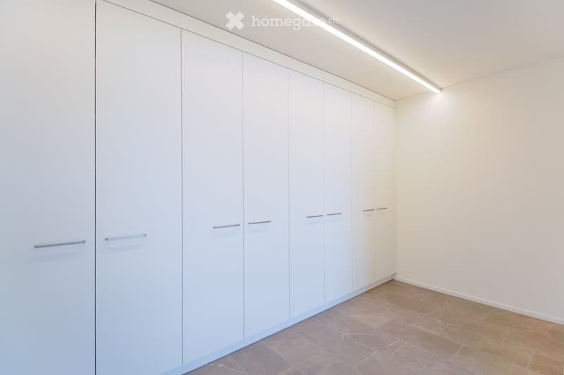 Empty room with white built-in wardrobes and a tiled floor.