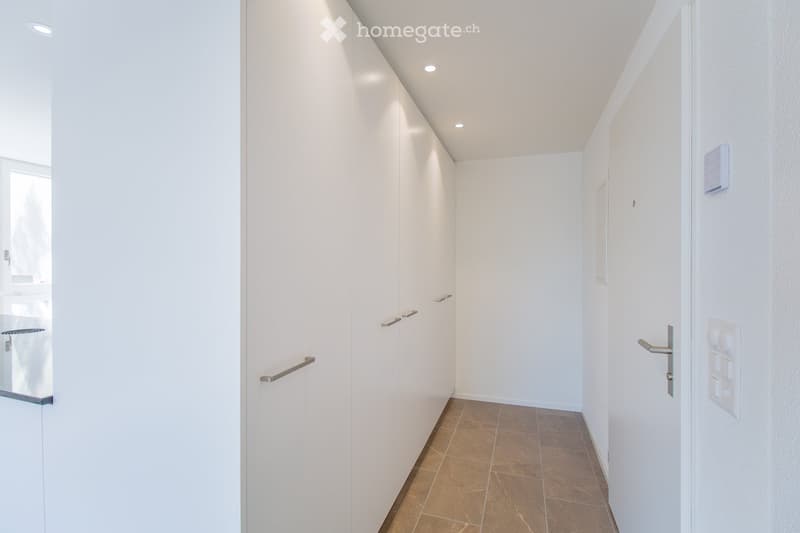 Modern, minimalist hallway with white walls, tiled floor, built-in white cabinets, and recessed lighting.