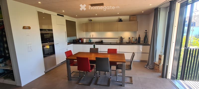 Modern kitchen with white cabinets, a wooden dining table with red and grey chairs, and various kitchen appliances and decor items on the counter.