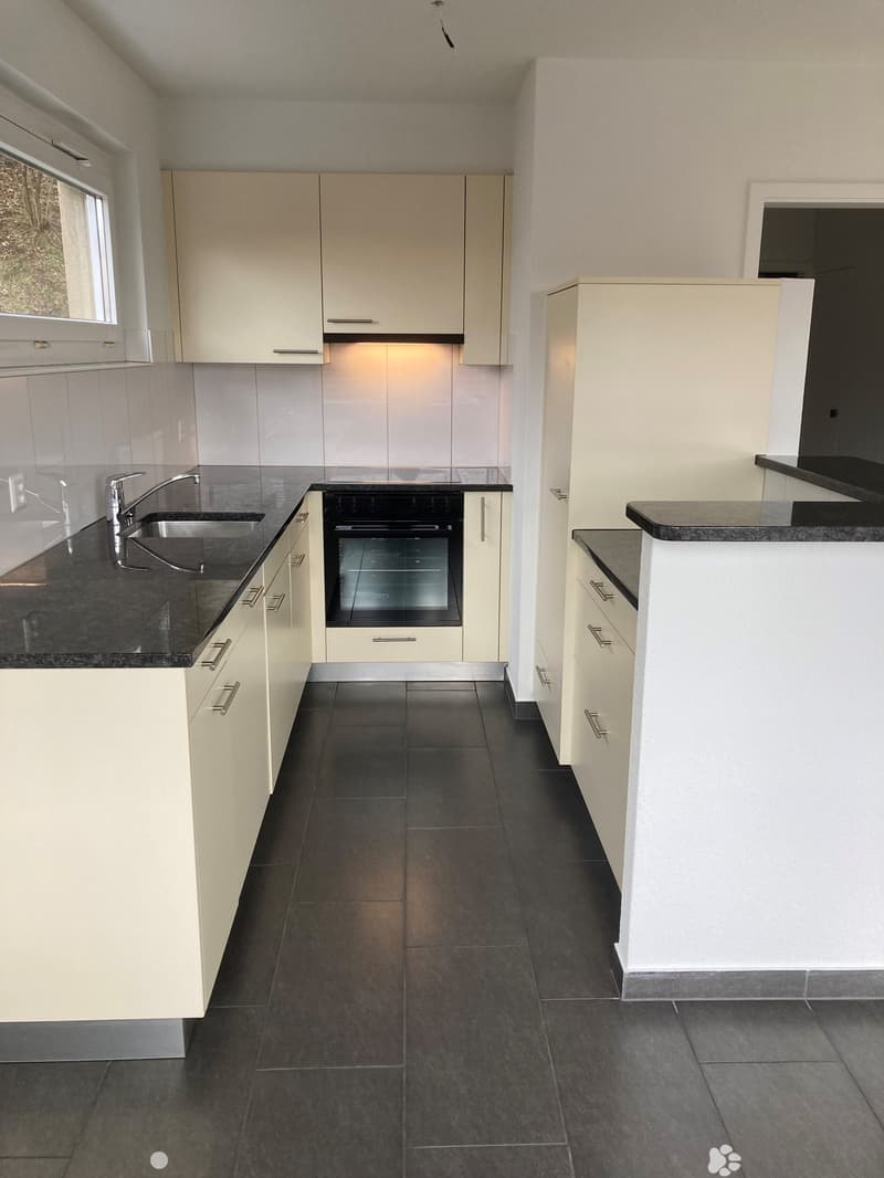 Modern kitchen with white cabinets, black countertops, and dark tiled flooring. Features a sink with a modern faucet and a built-in oven.