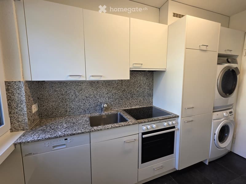 Modern kitchen with white cabinets, granite countertops, stainless steel sink, oven, dishwasher, and washing machine.