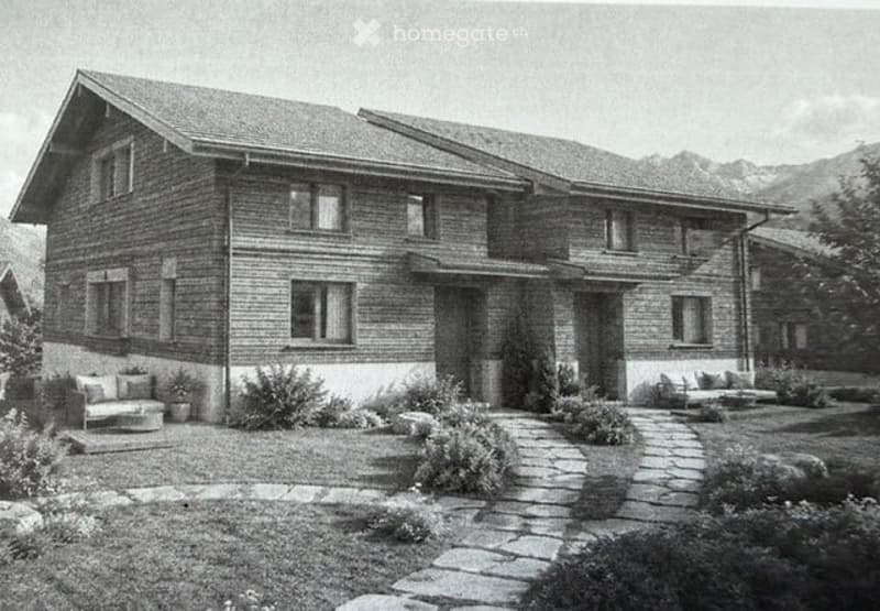 Two-story brick house with a sloped roof, multiple windows, and a stone pathway leading to the entrance. The house is surrounded by a well-maintained garden with shrubs and small seating areas.