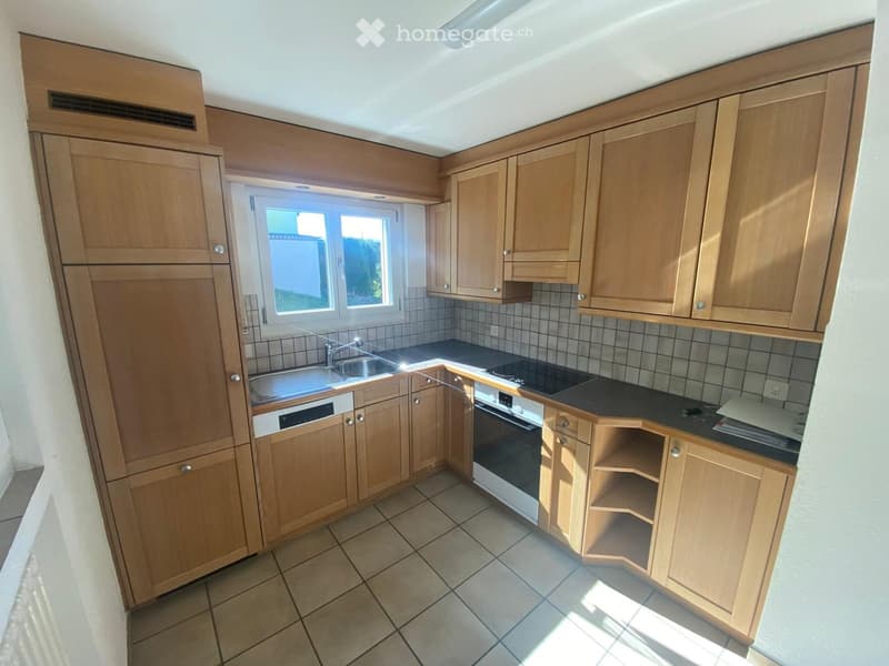 Modern kitchen with light wooden cabinets, tiled backsplash, and stainless steel appliances including a sink, oven, and dishwasher.