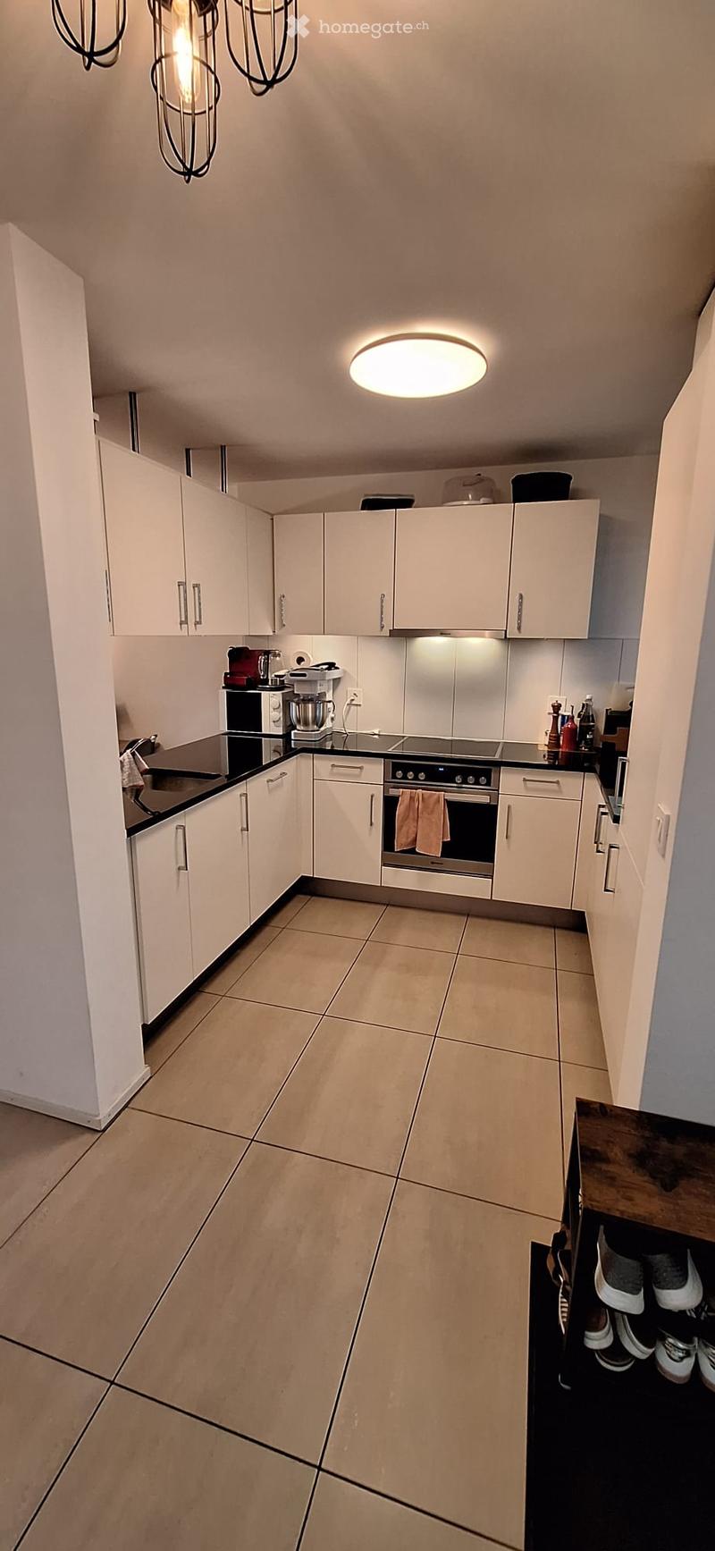 Modern kitchen with white cabinets, stainless steel appliances, and a black countertop. Features include a built-in oven, sink, and various small appliances.