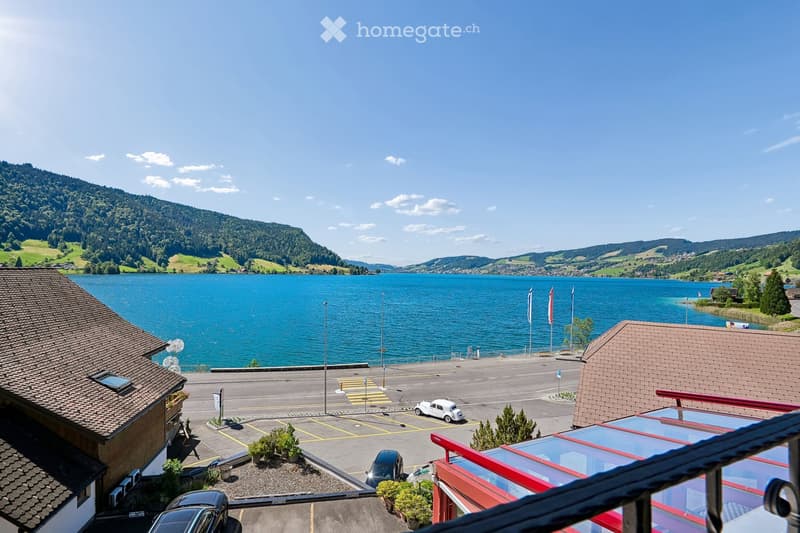View from a balcony overlooking a parking lot, lake, and surrounding mountains.