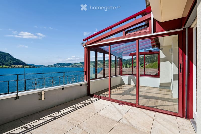 Balcony with large glass sliding doors, red frame, tiled floor, metal railing, and scenic lake view.