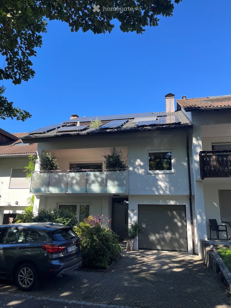 Two-story house with solar panels on the roof, a balcony, garage, and a parked car in front.