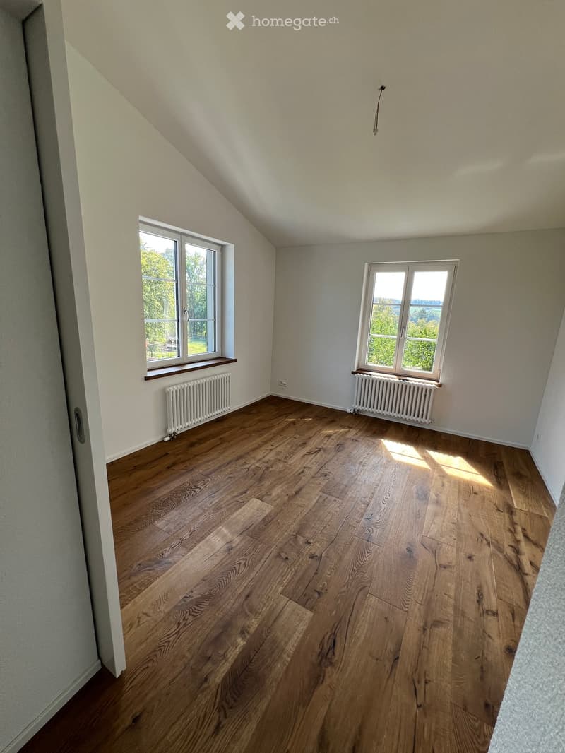 Empty room with wooden flooring, white walls, and two windows with radiators beneath them.