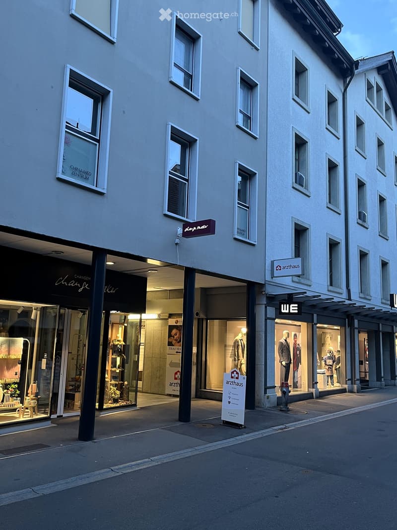 Multi-story building with multiple storefronts, including a clothing store and a medical center, with visible signage and mannequins in the windows.