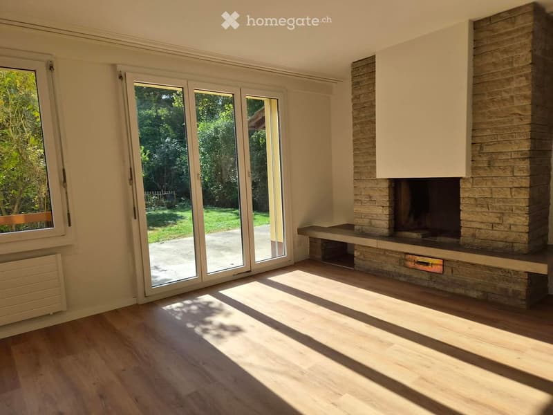 Bright living room with wooden flooring, large sliding glass doors leading to a garden, and a stone fireplace with a built-in bench.
