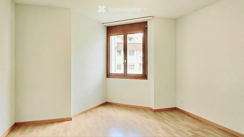Empty room with light-colored wooden flooring and white walls, featuring a single window with wooden frame and blinds.