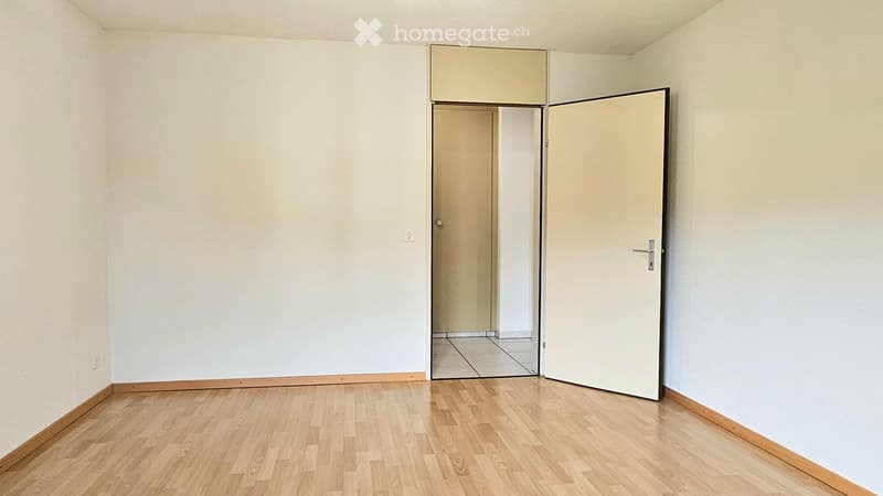 Empty room with wooden flooring, white walls, and a partially open door leading to another room.