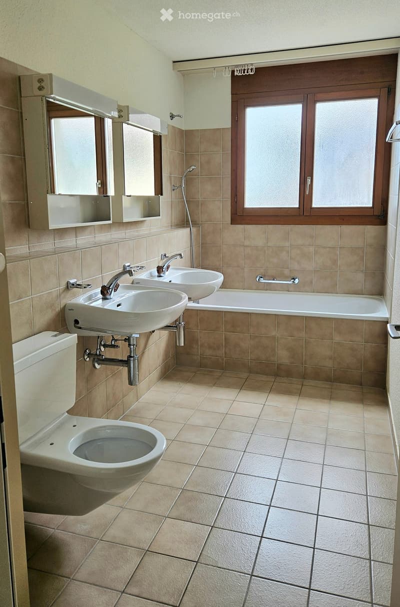 Bathroom with beige tiles, two sinks, a toilet, a bathtub, and a mirror above the sinks.