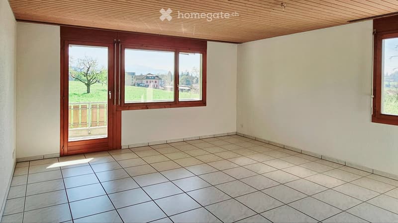 Empty room with tiled floor, white walls, large wooden-framed windows, and a sliding door leading to a balcony.
