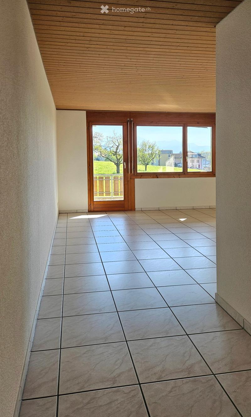 Empty hallway with tiled floor, wooden ceiling, and large window with double doors leading outside.
