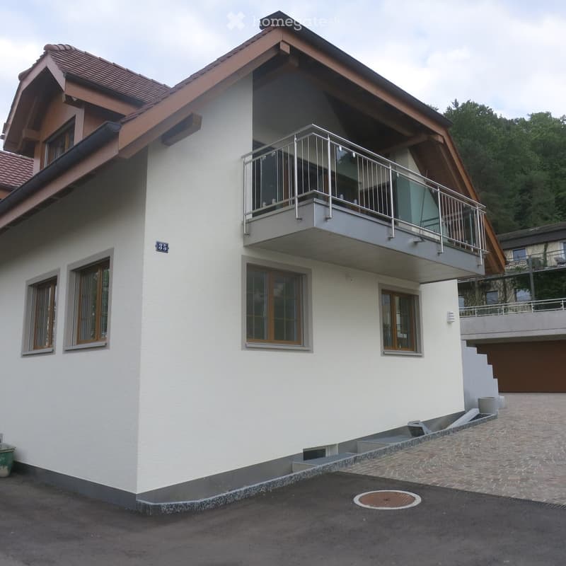 Two-story house with white exterior, wooden trim, large windows, and a balcony with metal railing on the upper level.