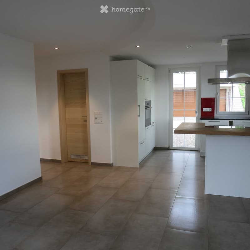 Empty kitchen with white cabinets, wooden floor, and a large window with a view of the garden.