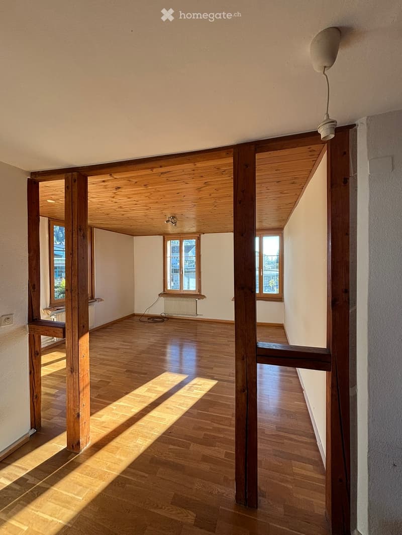 Empty room with wooden flooring, exposed wooden beams, and natural light from windows. No furniture or equipment present.
