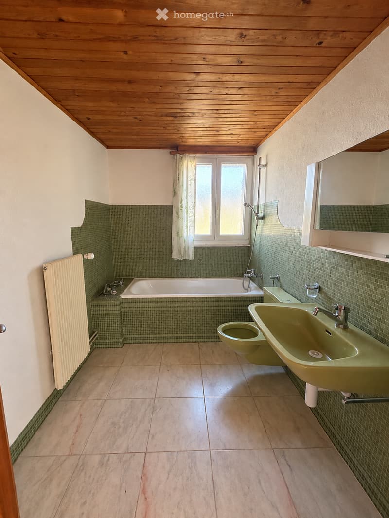 Bathroom with green tiled walls, wooden ceiling, marble floor, bathtub, sink, toilet, radiator, and mirror.