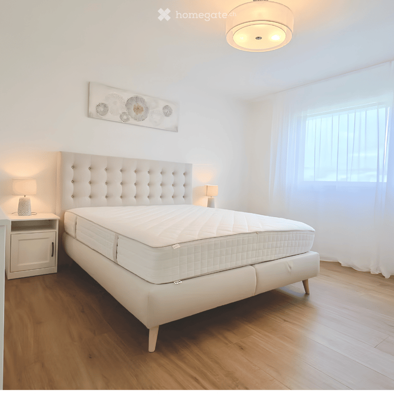 Modern bedroom with a large white upholstered bed, wooden nightstand, and a decorative wall art piece above the bed.