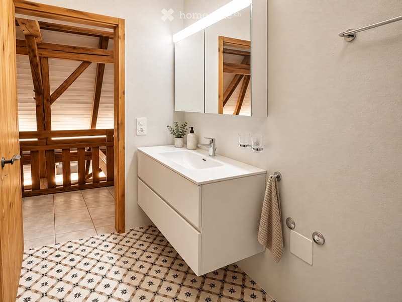 Modern bathroom with a white sink, mirror, and cabinet. Features a decorative patterned tile floor and a wooden door frame leading to another room.